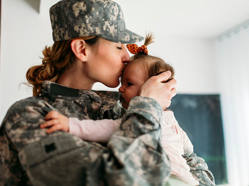 Army woman holding and kissing baby on forehead