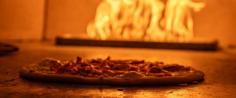 A pizza in a pizza oven with fire behind it.