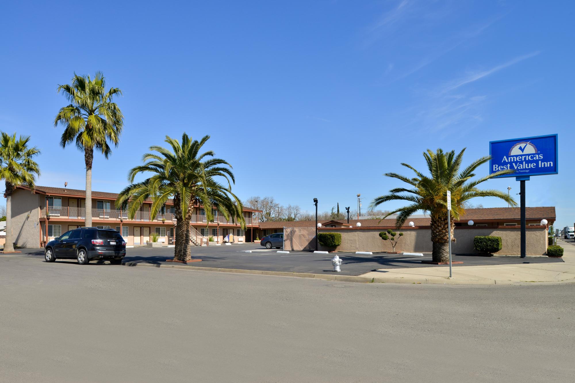 Street view of hotel exterior with palm trees and parking