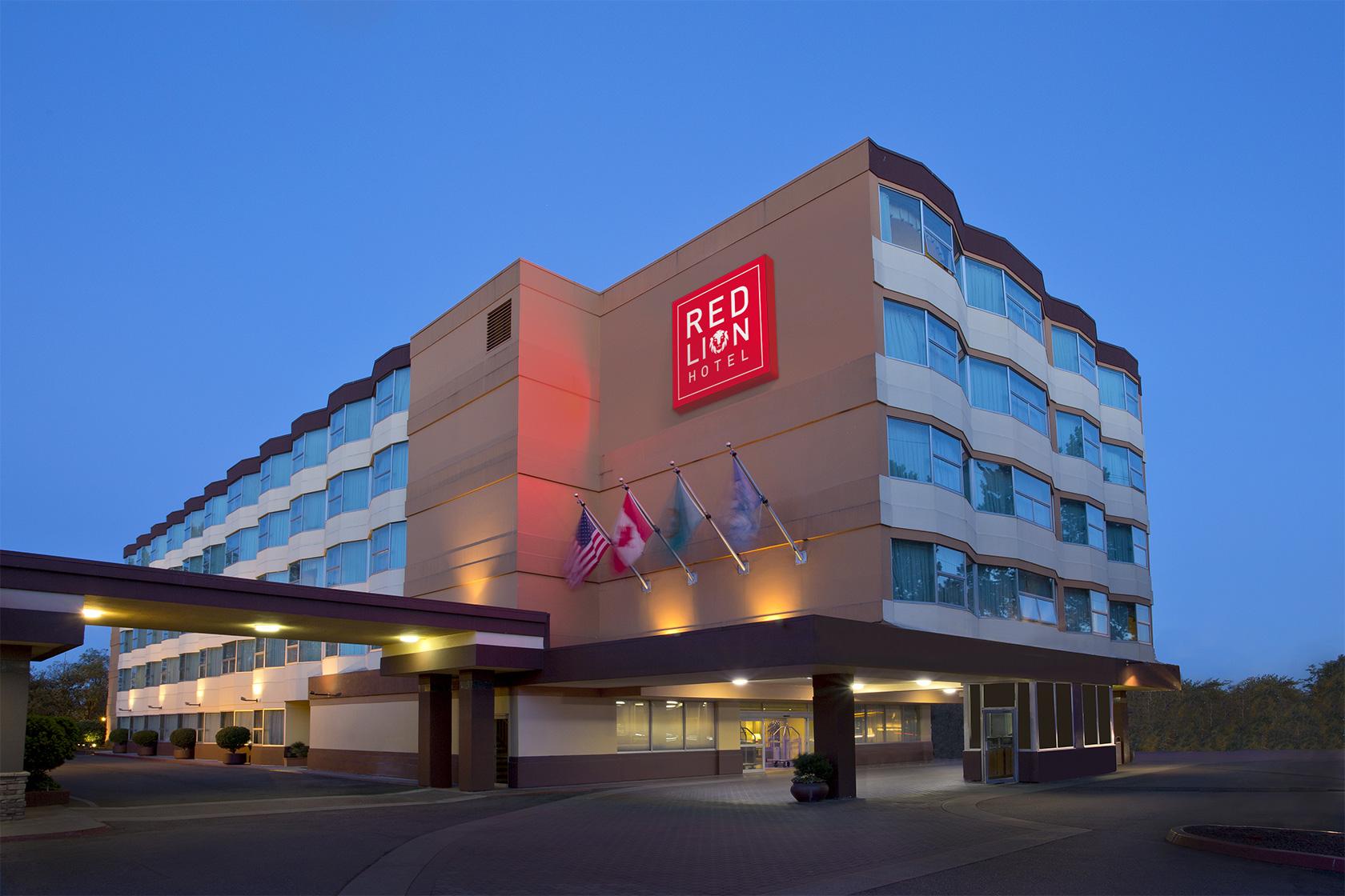 Hotel exterior at dusk with entrance to lobby, flags, and red sign
