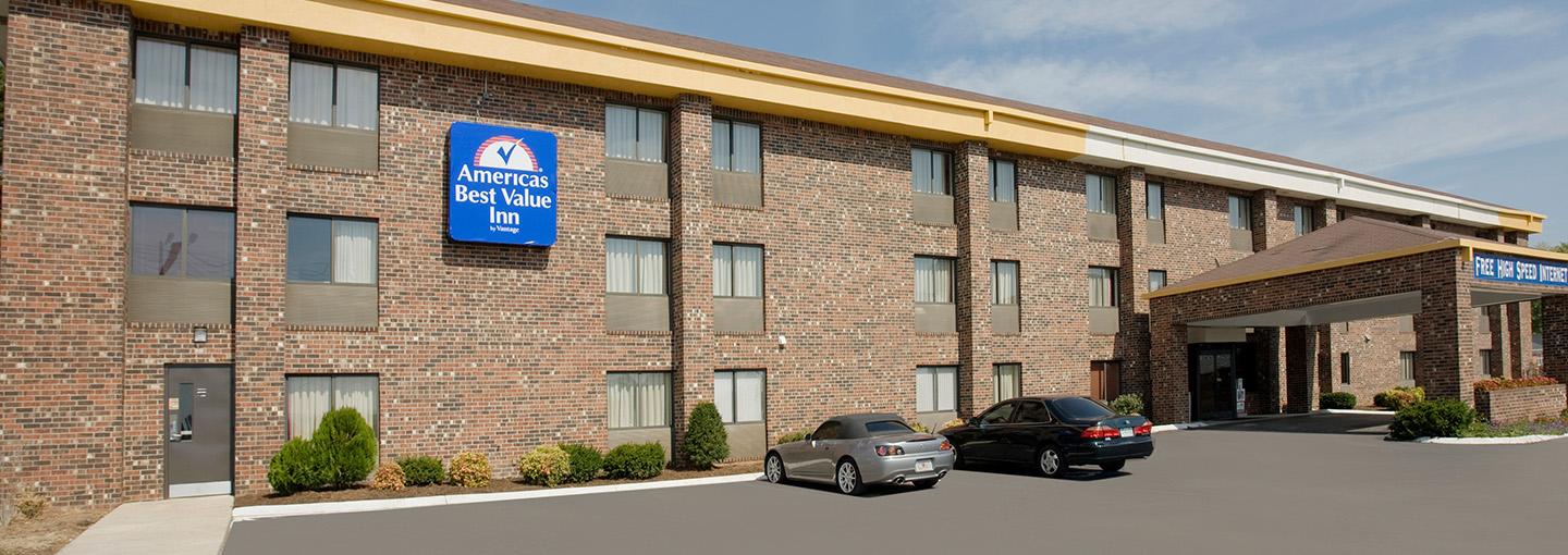 Hotel exterior with two cars in parking lot and blue Americas Best Value Inn sign