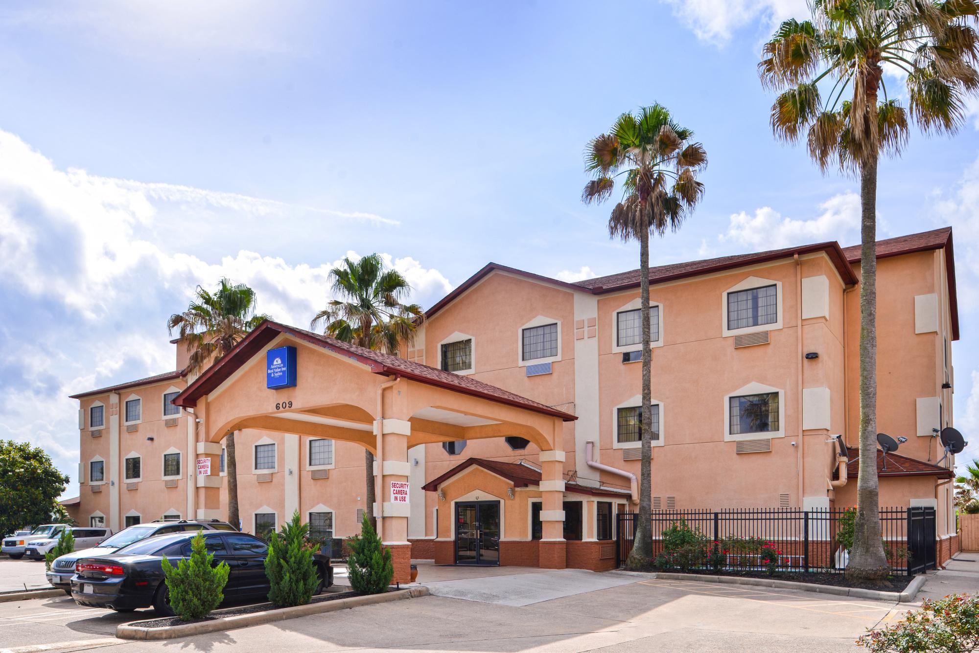 Hotel front exterior with parking and palm trees on a sunny day