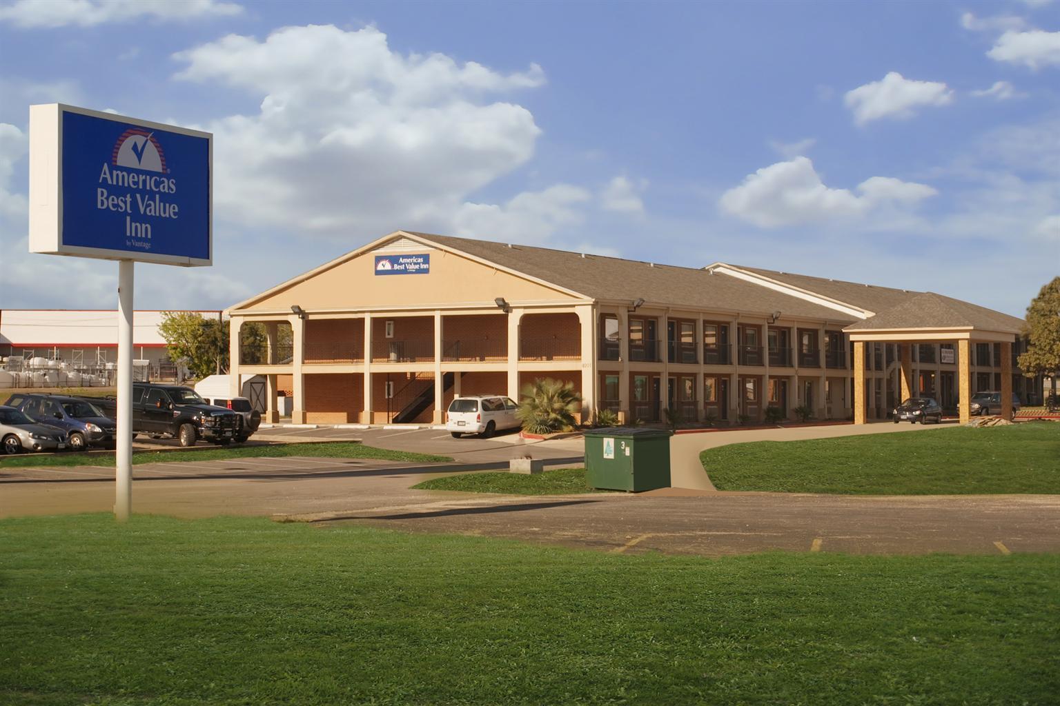 Street view of hotel exterior with parking, lawn, and sign
