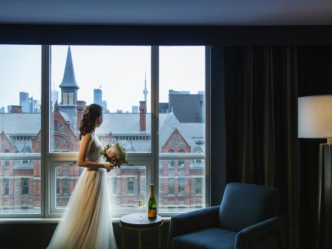 A bride looking out the window in a room at The Yorkville Royal Sonesta Hotel Toronto.