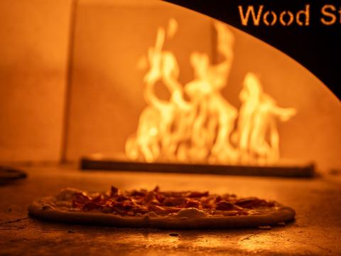 A pizza in a pizza oven with fire behind it at Certo! restaurant in Washington, D.C.