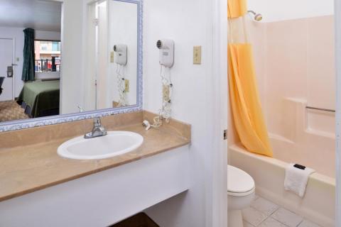 Clean, well lit guest room bathroom sink and bathtub