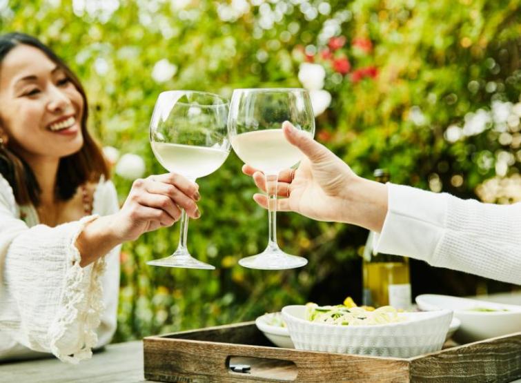 friends holding up wine glasses to cheers at outdoor dining setting